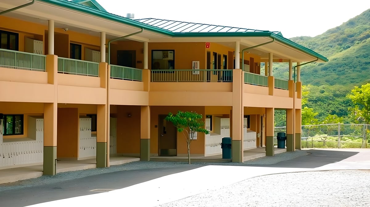 Das mehrstöckige Gebäude der Le Jardin Academy mit überdachtem Gehweg und Balkonen vor einer bergigen Landschaft.
