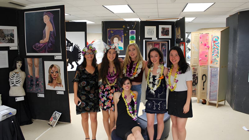 Eine Gruppe junger Schülerinnen der Le Jardin Academy steht zusammen in einer Kunstausstellung mit verschiedenen gerahmten Kunstwerken.