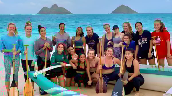 Eine Gruppe von Schülerinnen der Le Jardin Academy steht gemeinsam in Sportkleidung auf einem Boot vor einer Kulisse mit Inseln und türkisfarbenem Wasser.