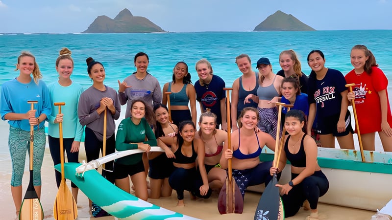 Eine Gruppe von Schülerinnen der Le Jardin Academy steht gemeinsam in Sportkleidung auf einem Boot vor einer Kulisse mit Inseln und türkisfarbenem Wasser.
