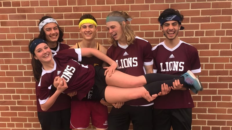 Eine Gruppe von Schülerinnen und Schülern in maroonfarbenen Lions-Trikots posiert vor einer Backsteinmauer auf dem Gelände der Leamington District Secondary School.