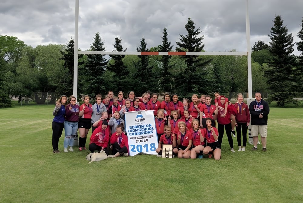 Eine große Gruppe von Schülern der Leduc Composite High School versammelt sich auf einem Fußballfeld mit Tor und umgeben von Kiefern.