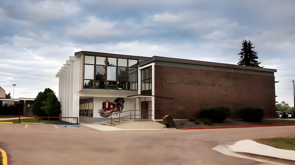 Das moderne mehrstöckige Backsteingebäude der Leduc Composite High School mit großen Fenstern und einer markanten Eingangstür ist von Bäumen umgeben.