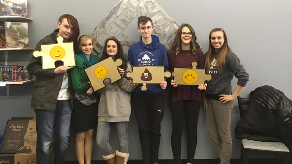 Eine Gruppe Schüler der Leduc Composite High School posiert mit bunten Schildern in einem Klassenraum mit Regalen und Kunstwerken im Hintergrund.