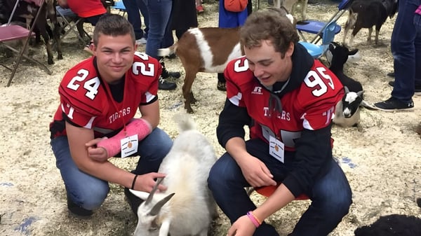 Zwei Schüler der Leduc Composite High School sitzen auf dem Boden und interagieren mit einem kleinen weißen Hund.