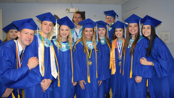Eine Gruppe von Absolventen in blauen Talaren feiert ihren Abschluss in einem Klassenraum der Lee Academy.