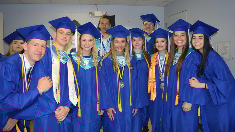 Eine Gruppe von Absolventen in blauen Talaren feiert ihren Abschluss in einem Klassenraum der Lee Academy.