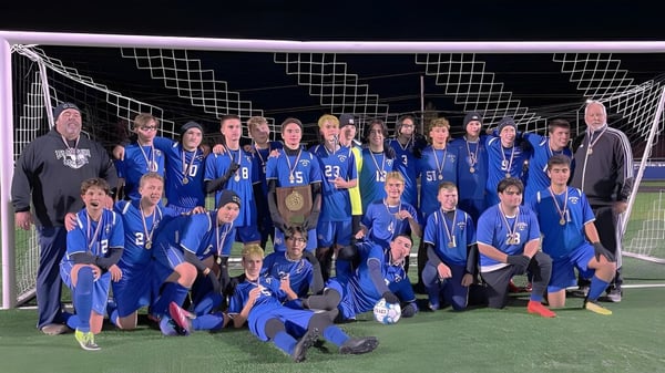 Schüler der Lee Academy feiern auf dem Fußballfeld ihren Sieg und halten einen Pokal.