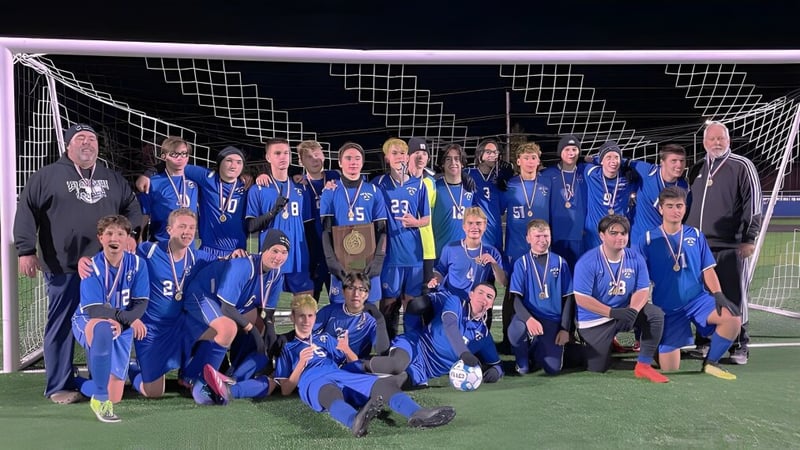 Schüler der Lee Academy feiern auf dem Fußballfeld ihren Sieg und halten einen Pokal.