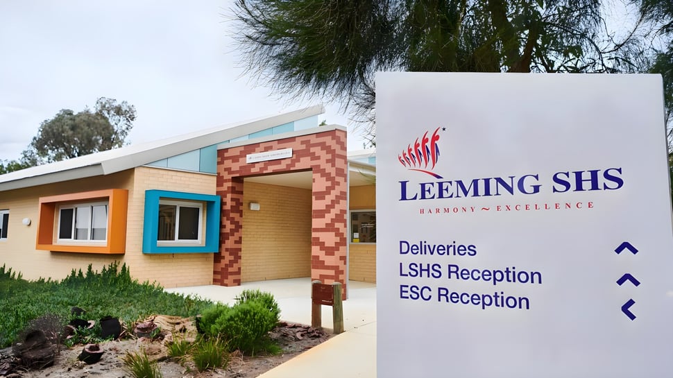 Das moderne eingeschossige Gebäude der Leeming Senior High School mit Backsteinfassade und beschriftetem Schild ist von Bäumen und Sträuchern umgeben.