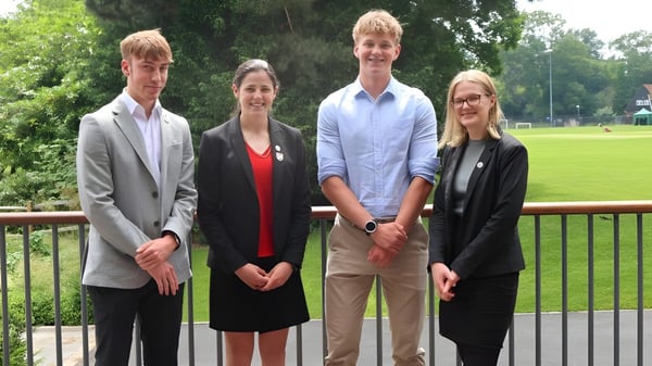 Vier Schülerinnen und Schüler der Leighton Park School stehen auf einem Balkon mit Blick auf einen grasbewachsenen Park.