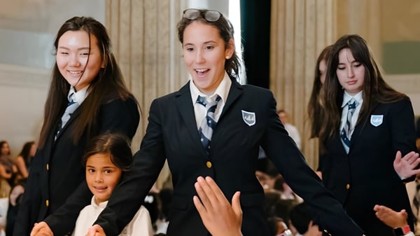 Eine Gruppe Schüler in Schuluniformen steht gemeinsam vor der Léman Manhattan Preparatory School in einem formellen Umfeld mit Säulen.