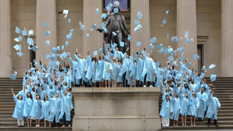 Schüler der Léman Manhattan Preparatory School versammeln sich in blauen Roben um eine große Statue auf einer Treppe.