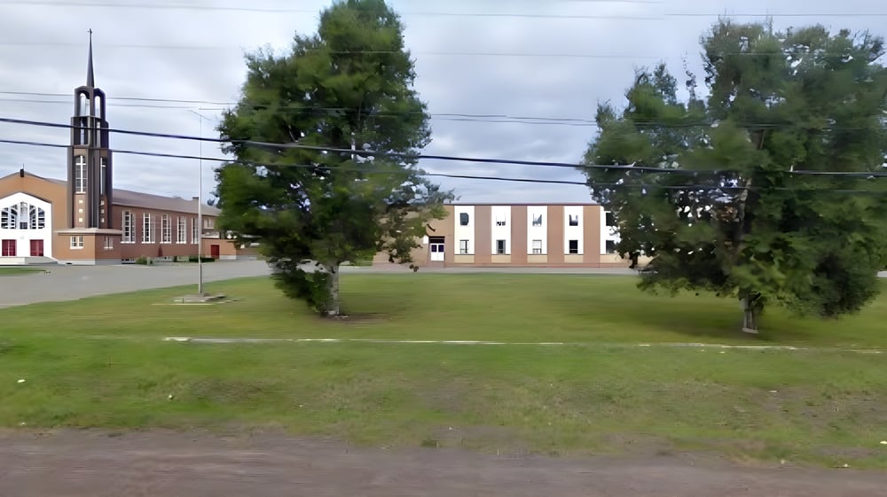 Das große Gebäude mit hohem Turm ist auf dem Gelände der Leo Burke Academy hinter einer Wiese mit Bäumen zu sehen.