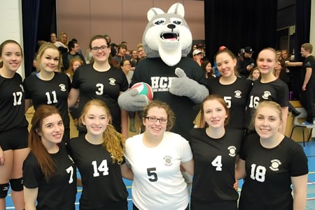 Eine Gruppe junger Sportlerinnen der Leo Burke Academy posiert zusammen mit dem großen weißen Maskottchen in der Sporthalle.
