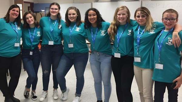 Eine Gruppe Schülerinnen mit grünen Shirts steht gemeinsam in einem Schulgebäude der Leo Burke Academy.