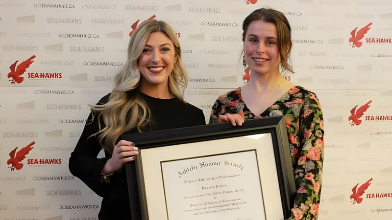 Zwei Schülerinnen der Leo Burke Academy halten ein gerahmtes Zertifikat vor einem Seahawks-Logo.