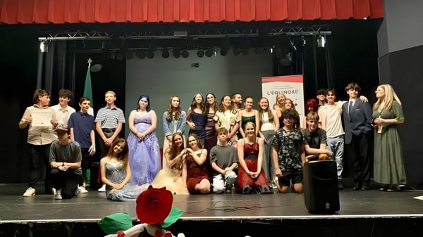 Eine Gruppe von Schülerinnen und Schülern steht in formeller Kleidung auf der Bühne der École élémentaire et secondaire publique L'Équinoxe vor einem roten Vorhang.
