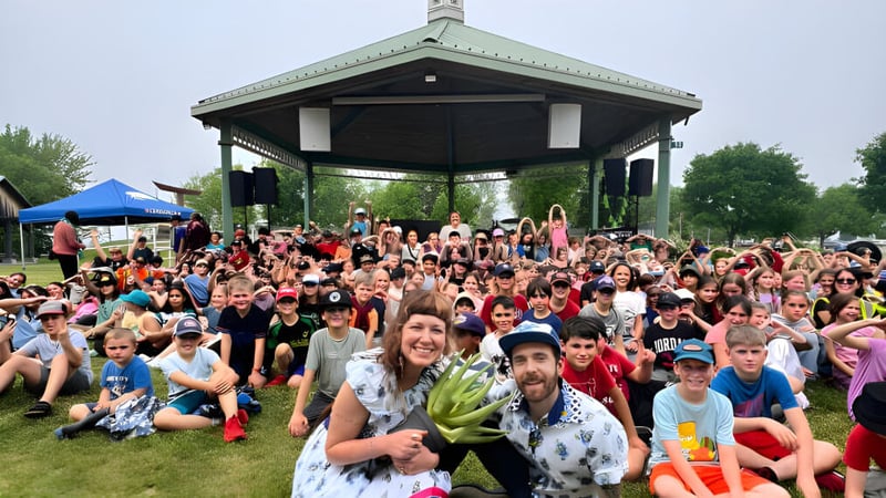 Eine Gruppe Schülerinnen und Schüler der École élémentaire et secondaire publique L'Équinoxe versammelt sich in einem Park mit einem Pavillon im Hintergrund.
