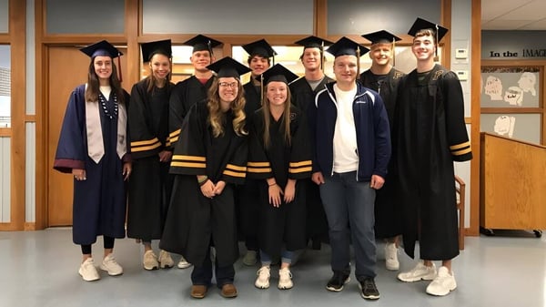 Eine Gruppe von Absolventinnen und Absolventen in der Abschlusskleidung auf dem Campus der Lester B. Pearson Catholic High School.