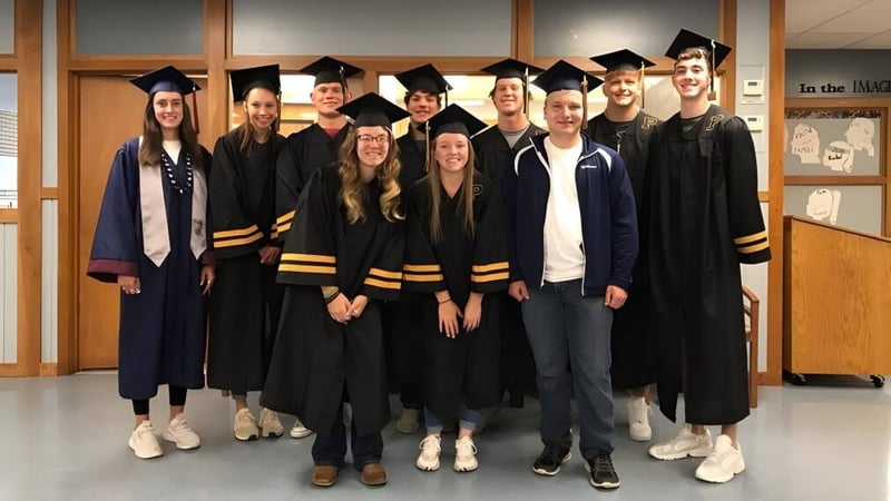 Eine Gruppe von Absolventinnen und Absolventen in der Abschlusskleidung auf dem Campus der Lester B. Pearson Catholic High School.