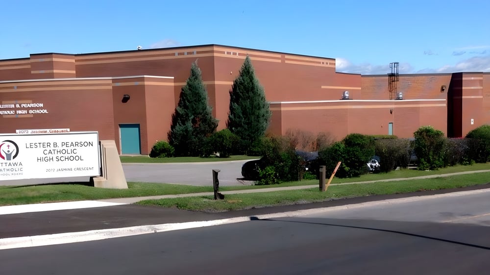 Das große Backsteingebäude der Lester B. Pearson Catholic High School mit einem Schild vor Bäumen und einem Parkplatz im Hintergrund.
