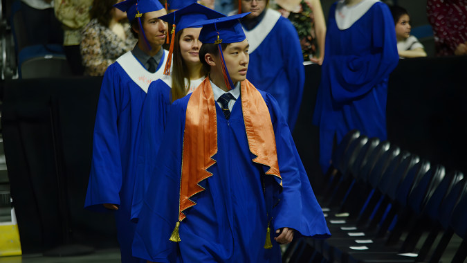 Eine Gruppe von Absolventinnen und Absolventen in blauen und orangen Roben bereitet sich auf der Abschlussfeier der Lethbridge School Division vor.