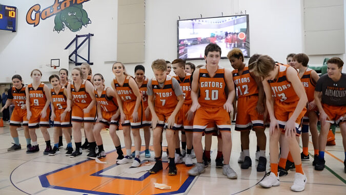 Eine Gruppe junger Basketballspieler in orangefarbenen Trikots steht gemeinsam auf dem Basketballfeld der Lethbridge School Division.