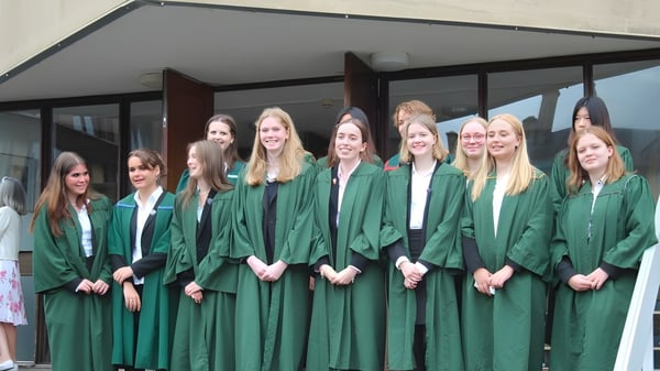 Eine Gruppe junger Absolventinnen der Leweston School steht in grünen Abschlussroben vor einem Gebäude mit überdachtem Durchgang.