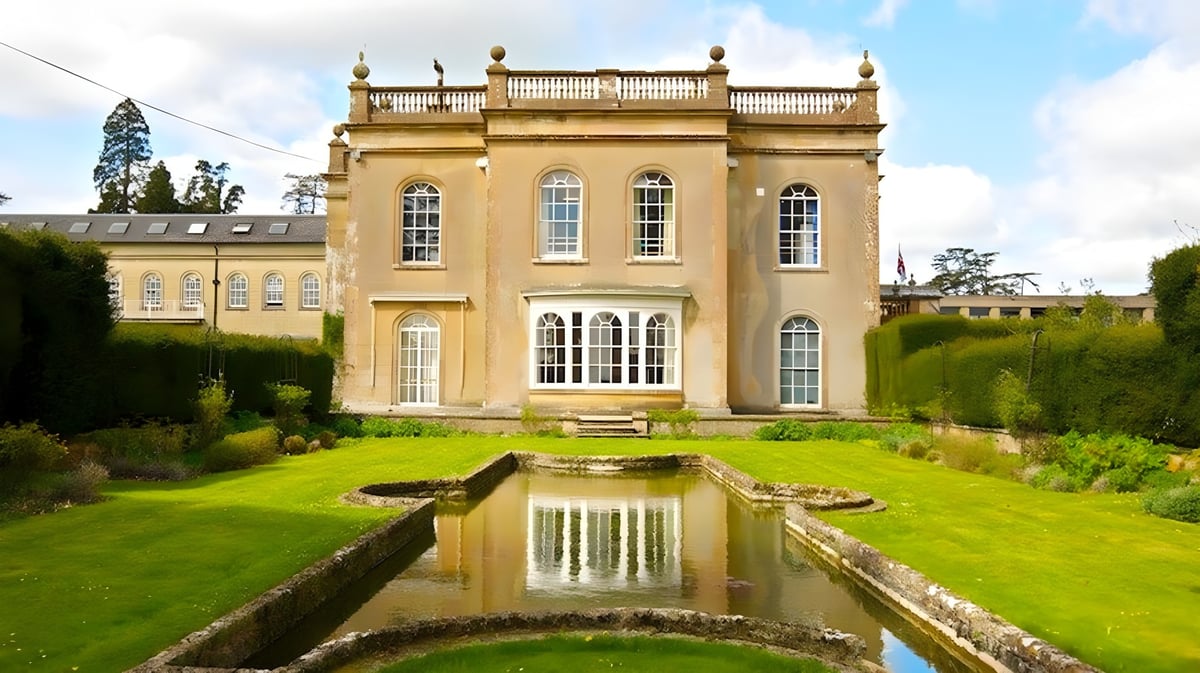 Das Gebäude der Leweston School steht in einem gepflegten Garten und spiegelt sich in einem ruhigen Teich wider.