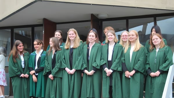 Eine Gruppe junger Schülerinnen der Leweston School steht in grünen Abschlussroben vor einem Gebäude mit überdachtem Durchgang.