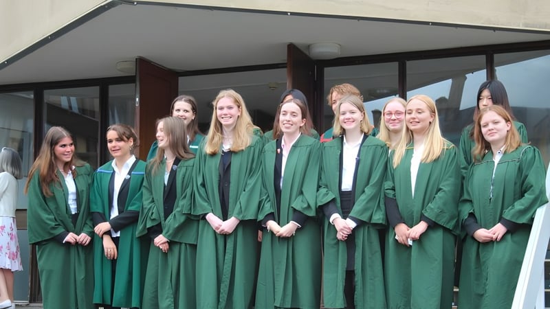 Eine Gruppe junger Schülerinnen der Leweston School steht in grünen Abschlussroben vor einem Gebäude mit überdachtem Durchgang.