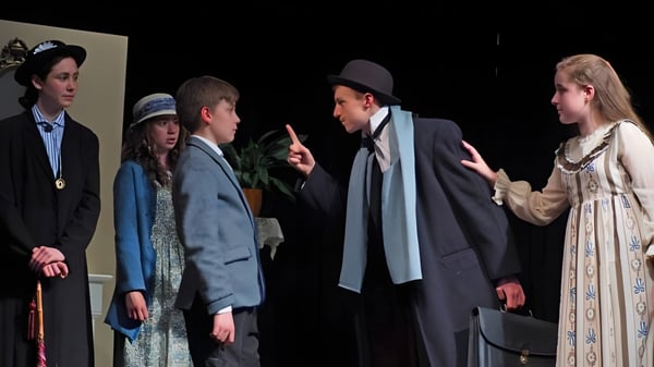 Schüler der Leweston School führen ein Theaterstück in historischen Kostümen auf einer dunklen Bühne auf.