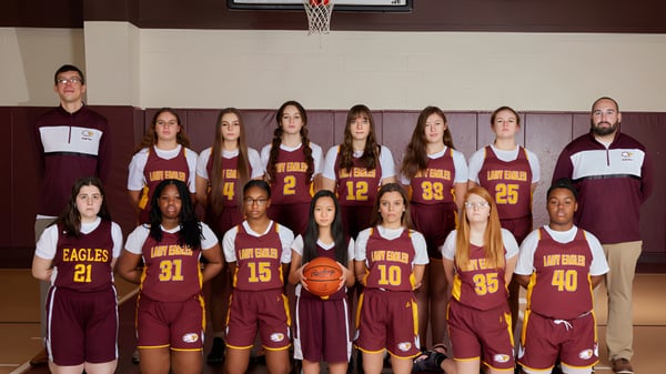 Eine Gruppe von Schülerinnen der Liberty Christian Academy posiert in Basketballtrikots in der Turnhalle vor dem Basketballkorb.