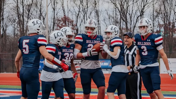 Eine Gruppe von Fußballspielern steht auf dem Feld der Liberty Christian Academy vor einem bewaldeten Hintergrund.