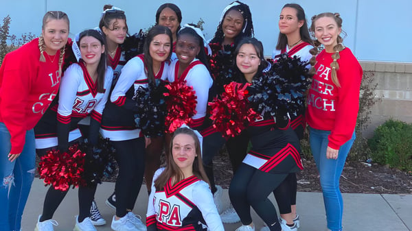 Eine Gruppe Cheerleader in roten und weißen Uniformen steht vor einer blauen Wand auf dem Campus der Life Prep Academy.