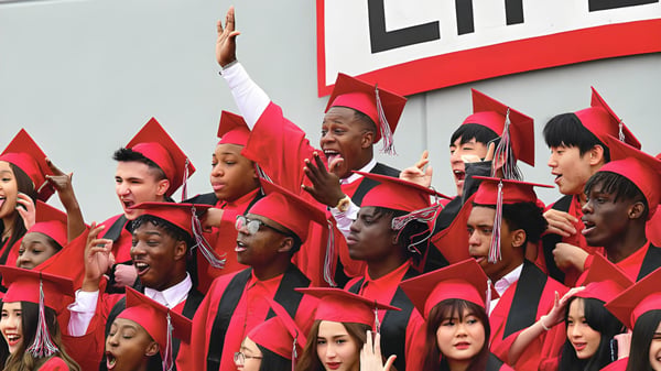 Eine Gruppe von Absolventen der Life Prep Academy in roten Talaren steht vor einem großen Life-Schild und feiert ihren Abschluss.