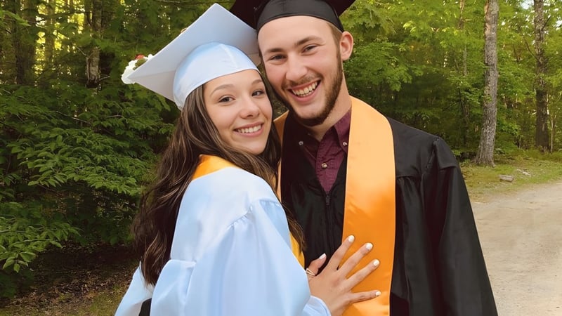 Zwei Absolventinnen der Lincoln Academy in Abschlusskleidung stehen zusammen in einem bewaldeten Bereich mit üppigem Grün.