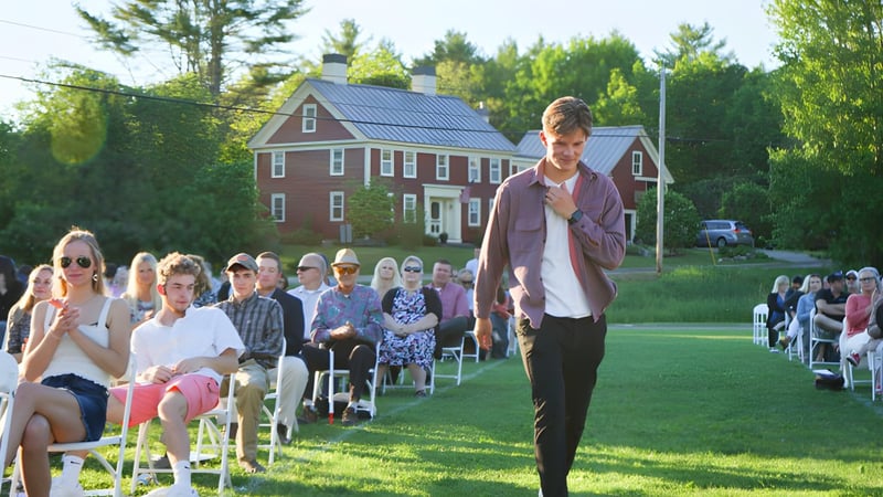 Eine Gruppe von Personen sitzt auf Stühlen auf einer Wiese vor dem roten Backsteinhaus der Lincoln Academy.