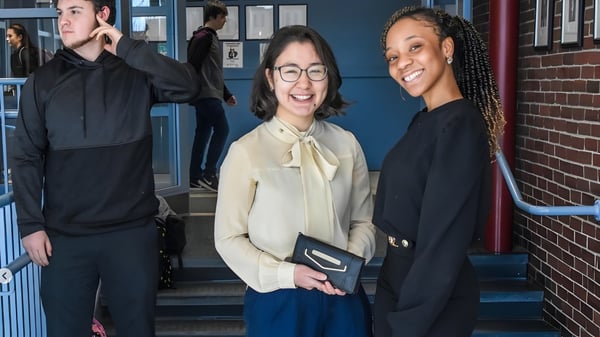 Drei Personen stehen auf einer Treppe vor einem Backsteingebäude auf dem Campus der Lincoln Academy.
