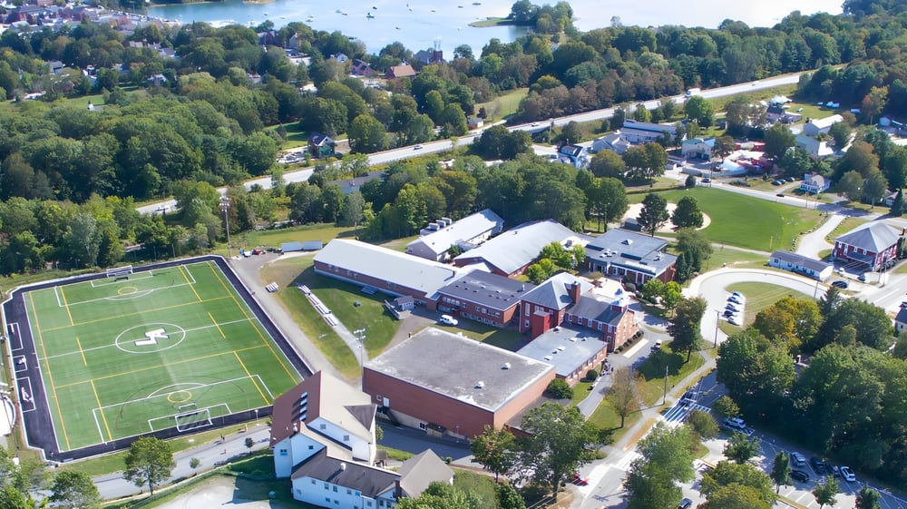 Luftaufnahme der Lincoln Academy mit Sportplatz und Gebäuden umgeben von grünen Wäldern.