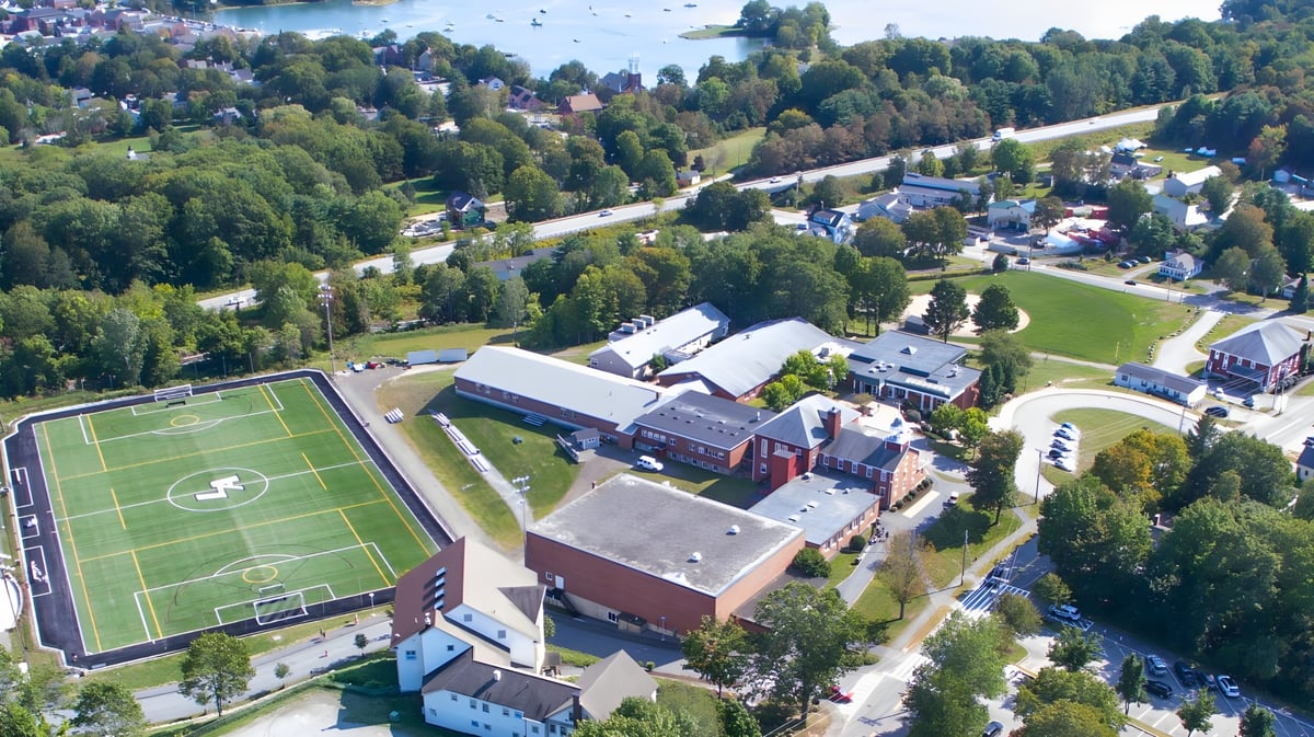 Luftaufnahme der Lincoln Academy mit Sportplatz und Gebäuden umgeben von grünen Wäldern.