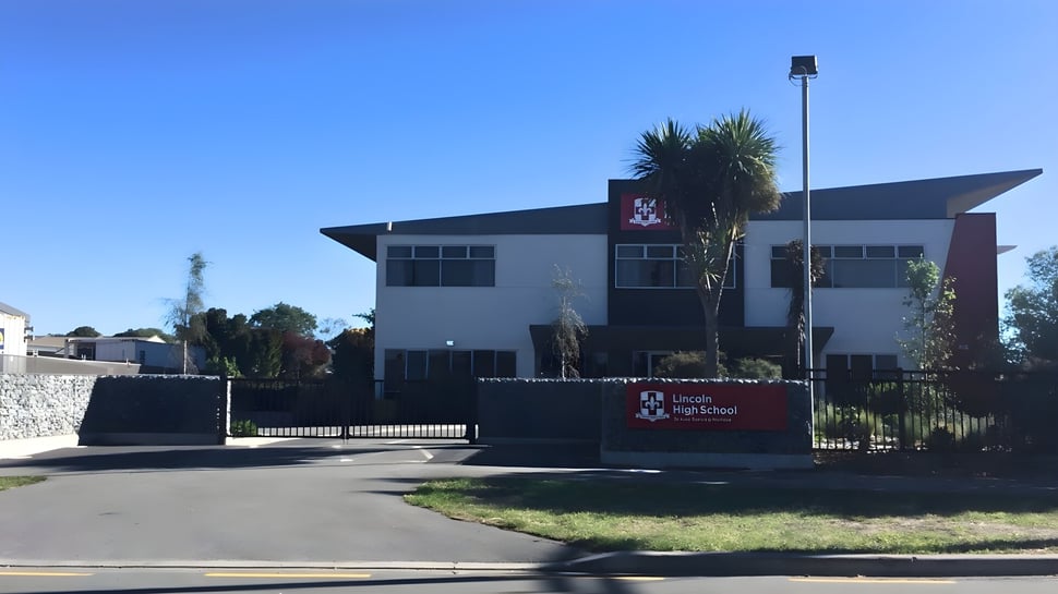 Das moderne Schulgebäude der Lincoln High School mit dem Logo und Eingangsbereich vor klarem Himmel.