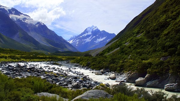 Ein grünes Tal mit einem fließenden Bach und schneebedeckten Bergen im Hintergrund, nahe der Lincoln High School.