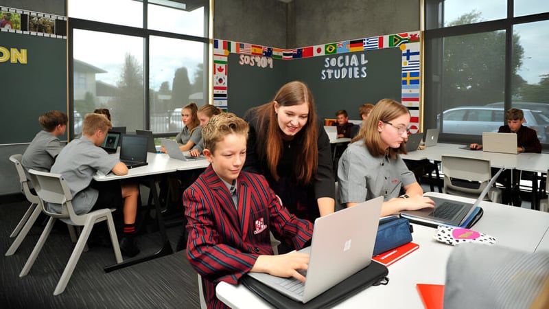 Schüler der Lincoln High School arbeiten in einem Klassenzimmer mit Laptops und internationalen Flaggen im Sozialkundeunterricht.