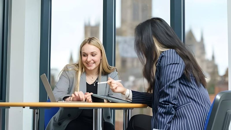 Zwei Frauen stehen vor einem Fenster mit Stadtblick auf dem Campus der Lincoln Minster School und führen ein Gespräch.