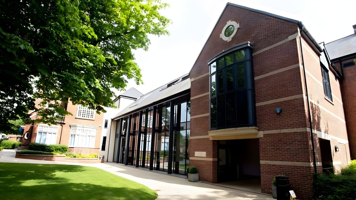 Das Backsteingebäude der Lincoln Minster School steht vor einer grünen Wiese und ist von Bäumen umgeben.