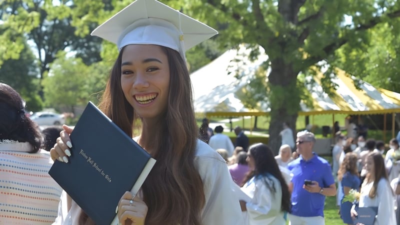 Eine Absolventin der Linden Hall trägt Kappe und Talar und hält ihr Diplom bei der Abschlussfeier im Freien.