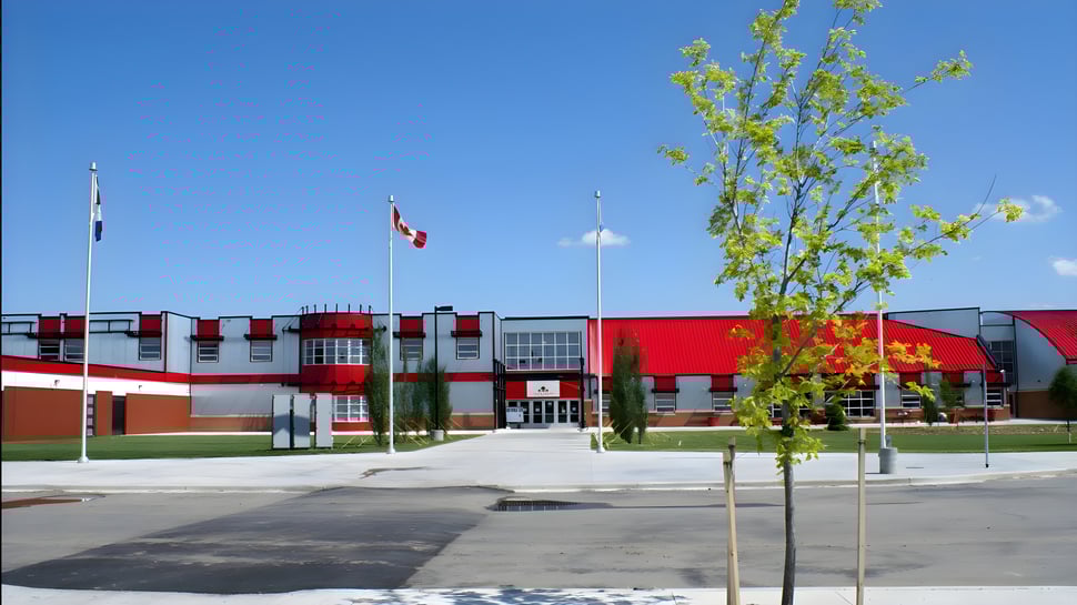 Das moderne Gebäude der Lindsay Thurber Comprehensive High School mit wehenden Fahnen und Bäumen im Vordergrund.