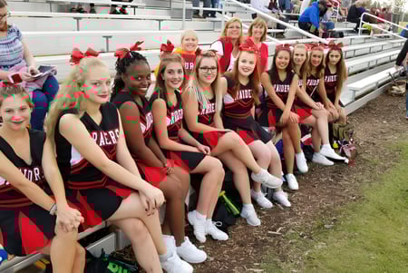 Eine Gruppe junger Cheerleaderinnen in roten und schwarzen Uniformen sitzt auf den Tribünen der Lindsay Thurber Comprehensive High School.